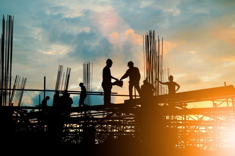 Imagem contra luz que mostra silhuetas de trabalhadores da construção civil durante uma obra