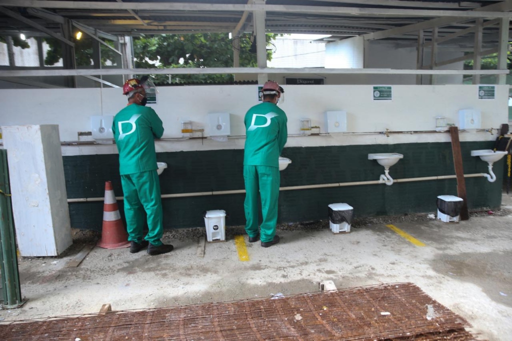 Foto mostra dois trabalhadores da construção civil higienizando as mãos em pias instaladas em canteiro de obra.